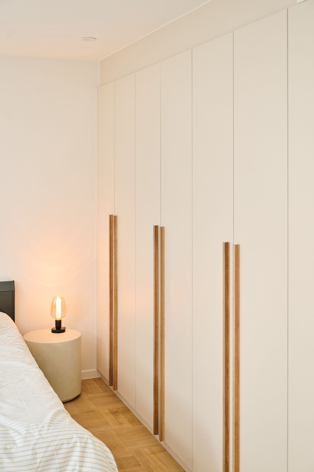 Beige maatkast met lange houten grepen naast bed met brandend nachtlampje