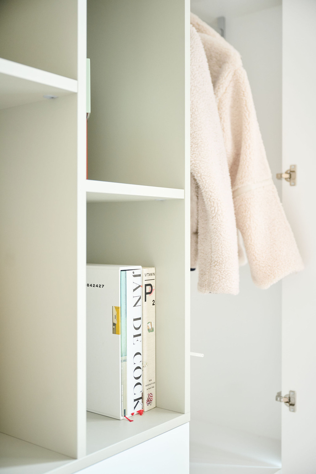 Détail d’une armoire blanche sur mesure avec livres décoratifs et manteau suspendu dans une entrée moderne