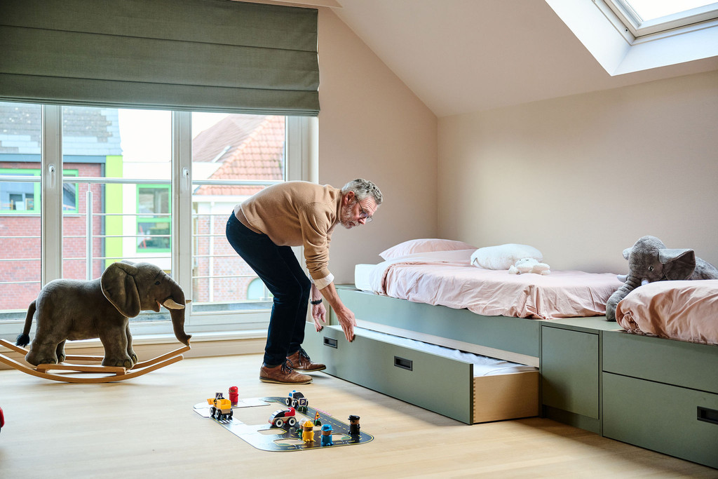Homme ouvrant un tiroir de rangement sous un lit d’enfant vert sur mesure dans une chambre lumineuse