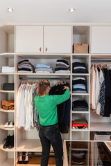 Femme choisit des vêtements dans un dressing blanc ouvert sur mesure avec étagères penderies et éclairage intégré