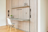 Bureau pliable sur mesure avec étagère en bois, plante en pot, et une chaise blanche, dans une pièce lumineuse.