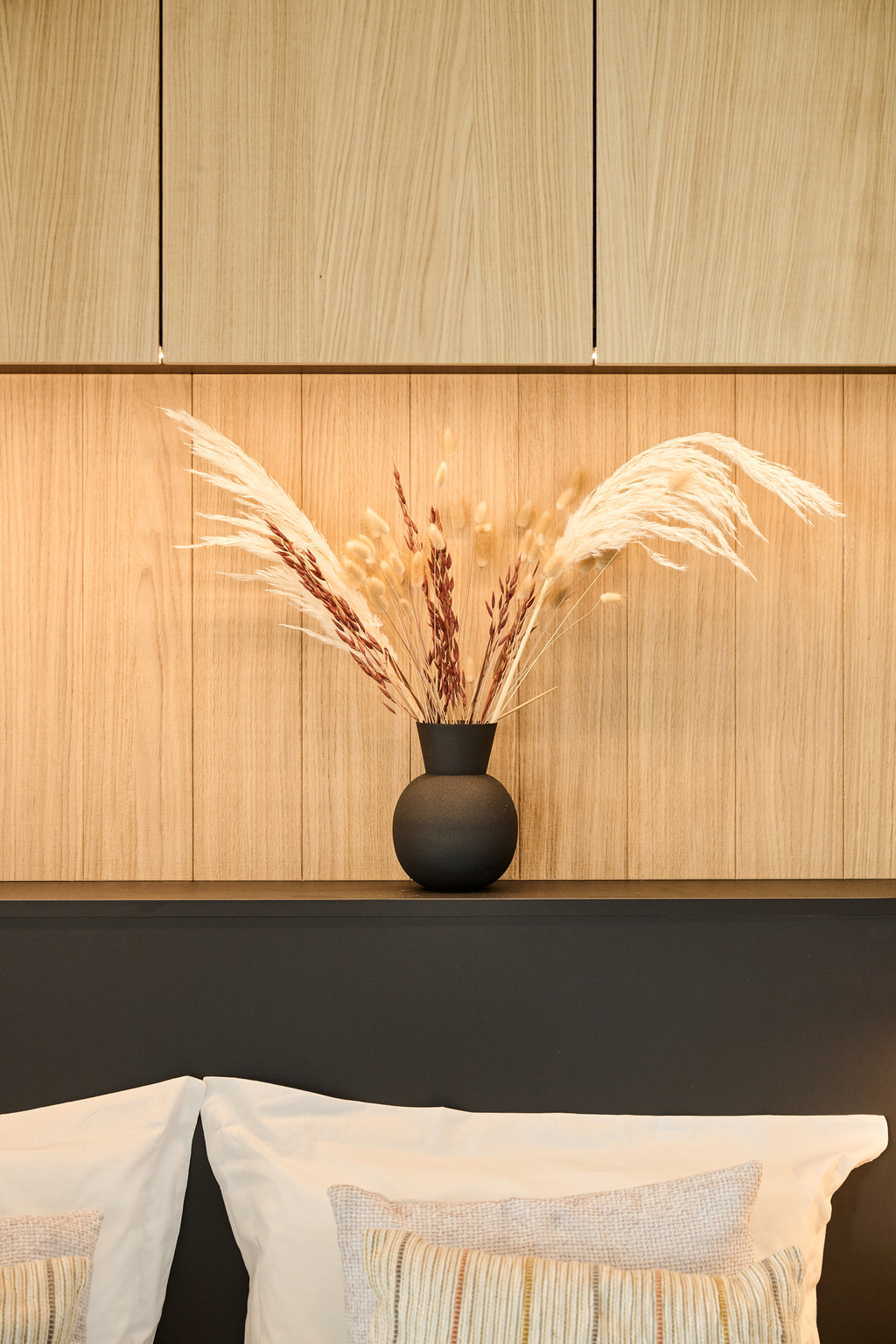 Détail de la tête de lit avec vase noir et arrangement floral naturel.