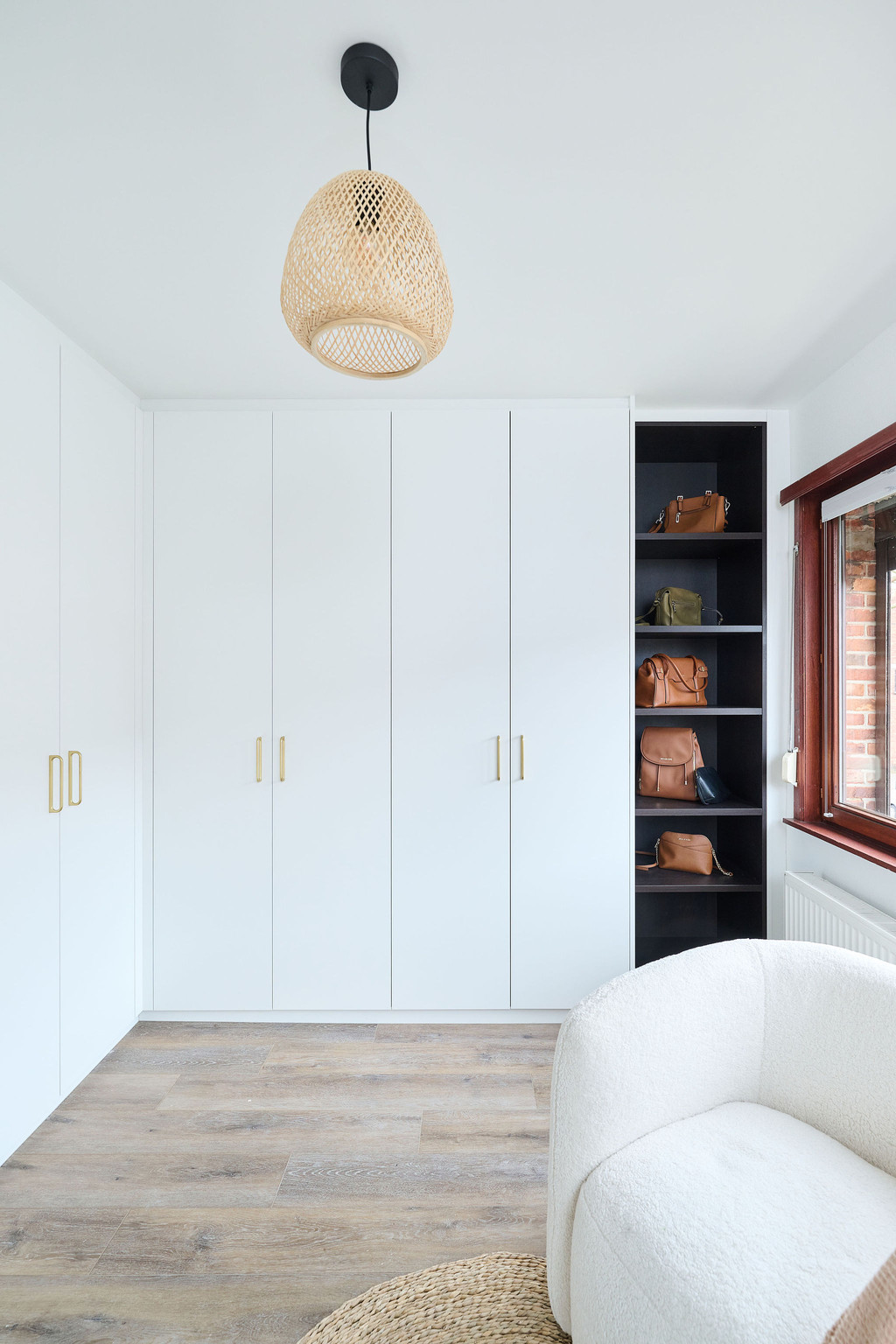 Dressing fermé sur mesure avec portes blanches et poignées dorées, accompagné d’étagères noires ouvertes pour le rangement des sacs à main.