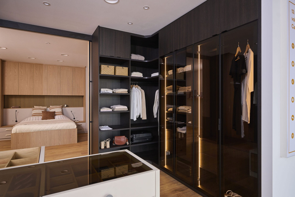 Dressing sur mesure avec portes vitrées, penderie et éclairage LED intégré en bois foncé dans un showroom