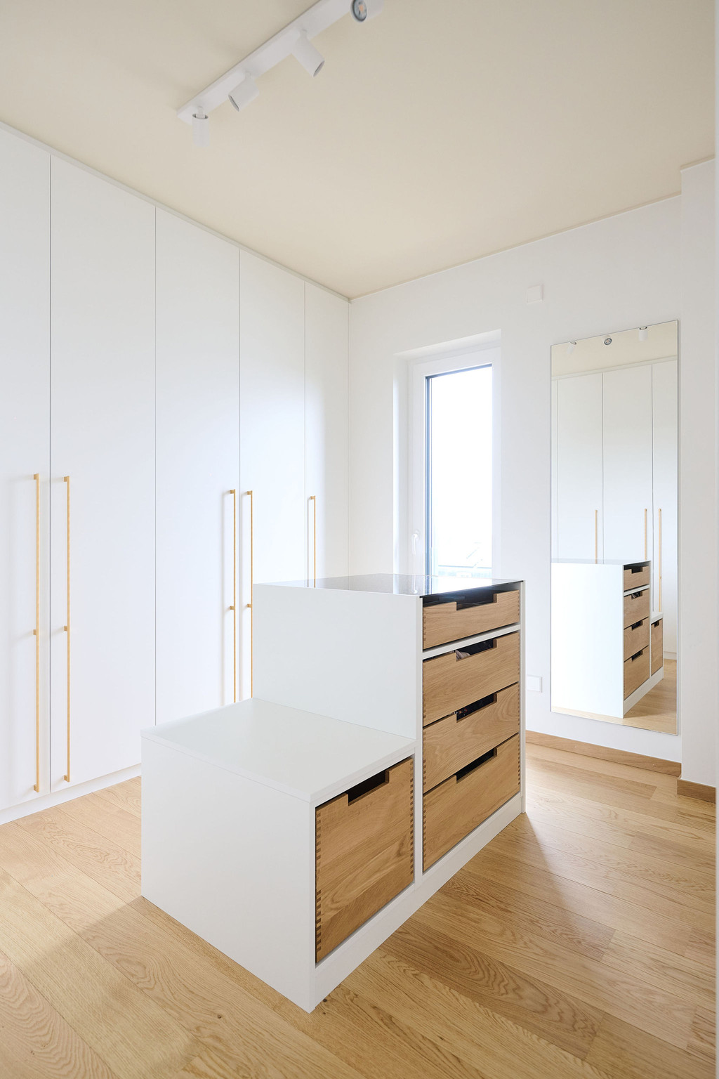 Maatwerk dressing met kasten in lichte tinten en een centraal lade-eiland in houtafwerking, voor een praktische en overzichtelijke indeling