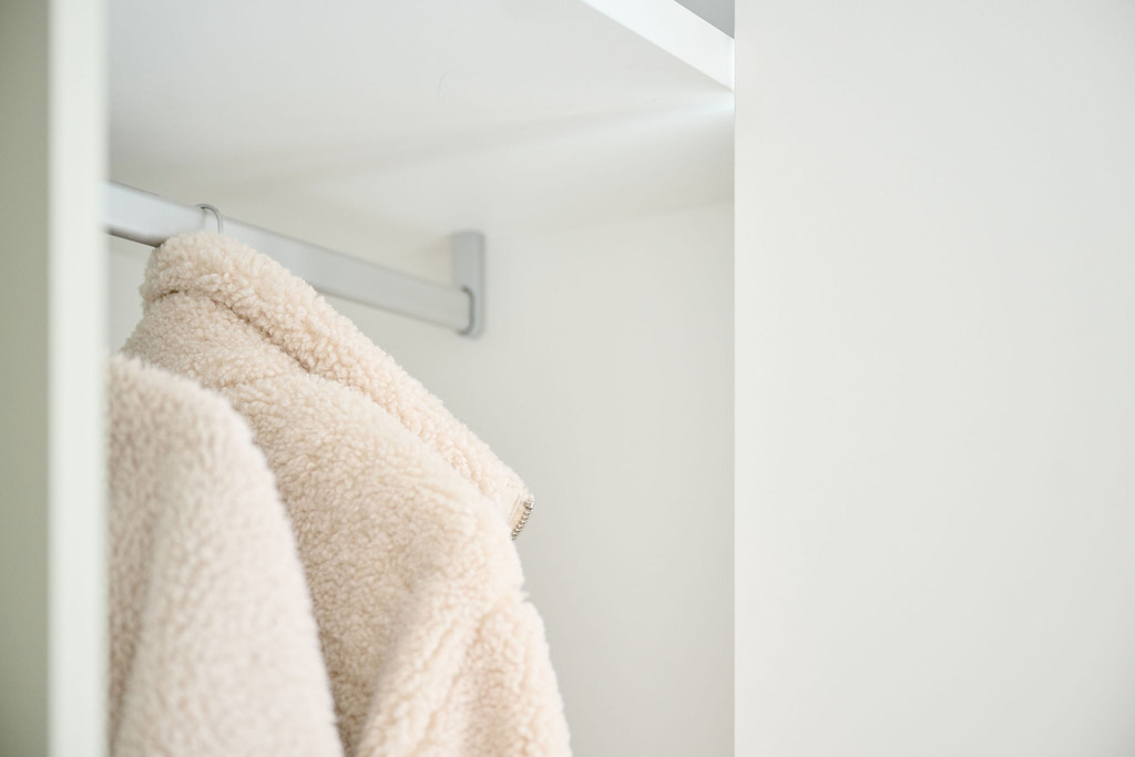 Gros plan sur un manteau clair suspendu à une tringle dans une armoire d’entrée blanche sur mesure
