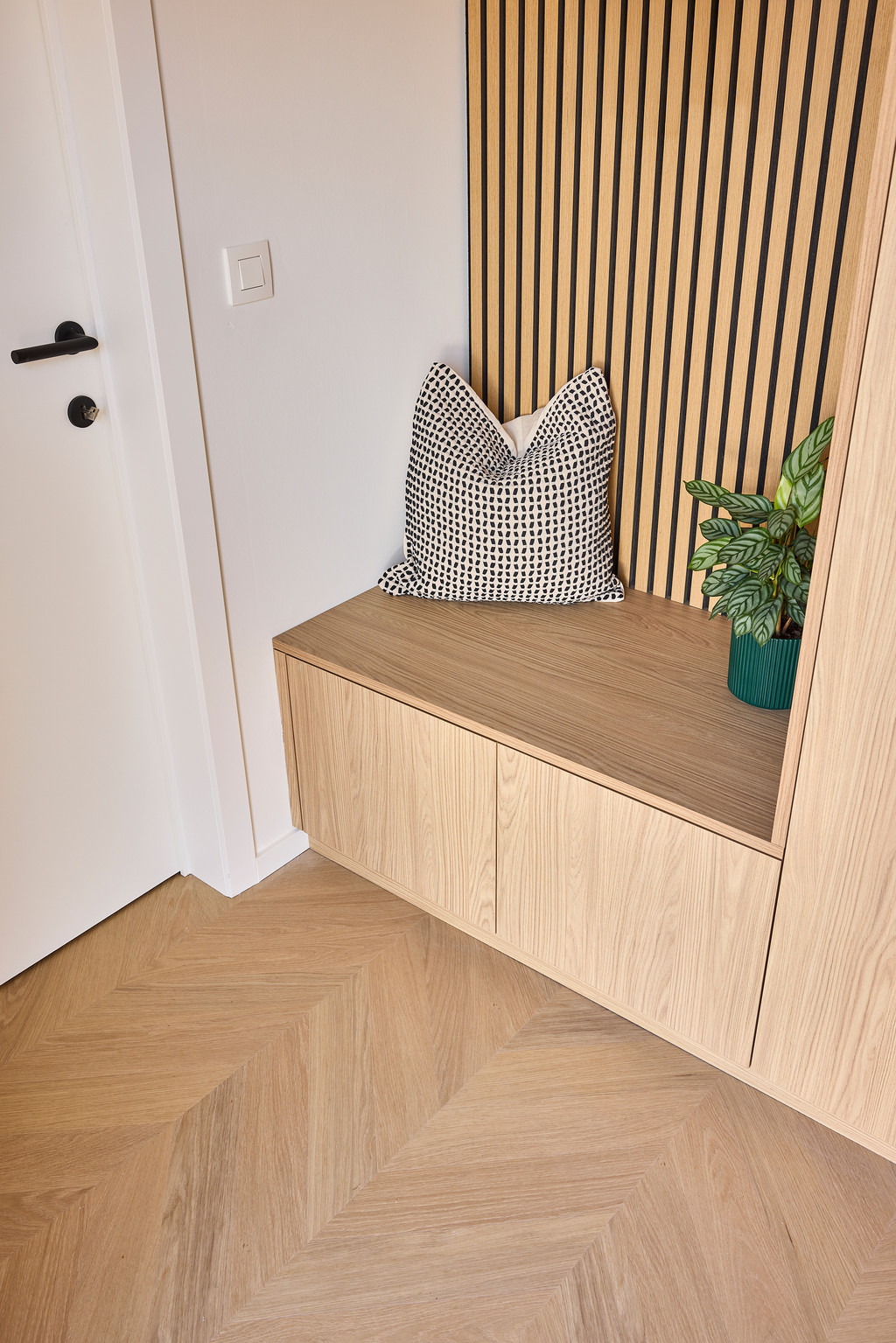 Detail van een houten zitbank op maat met geïntegreerde opbergruimte en houten lattenwand, voor extra warmte en functionaliteit in de inkomhal