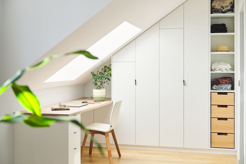Rangement sous toit sur mesure avec bureau et étagères, comprenant des tiroirs et des étagères ouvertes pour vêtements.