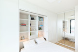 Opklapbed met op maat gemaakte kast met open rekken en verlichting, witte afwerking in een moderne slaapkamer.