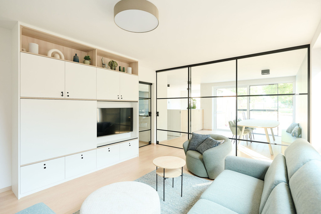 Meuble sur mesure blanc avec télévision et niches ouvertes dans un salon lumineux avec portes vitrées