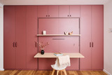 Opklapbed in roze kast met geïntegreerd bureau en decoratieve plank in kamer.