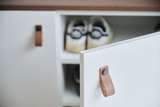 Détail d'un meuble de vestiaire sur mesure avec une poignée en cuir et des étagères pour ranger des chaussures.