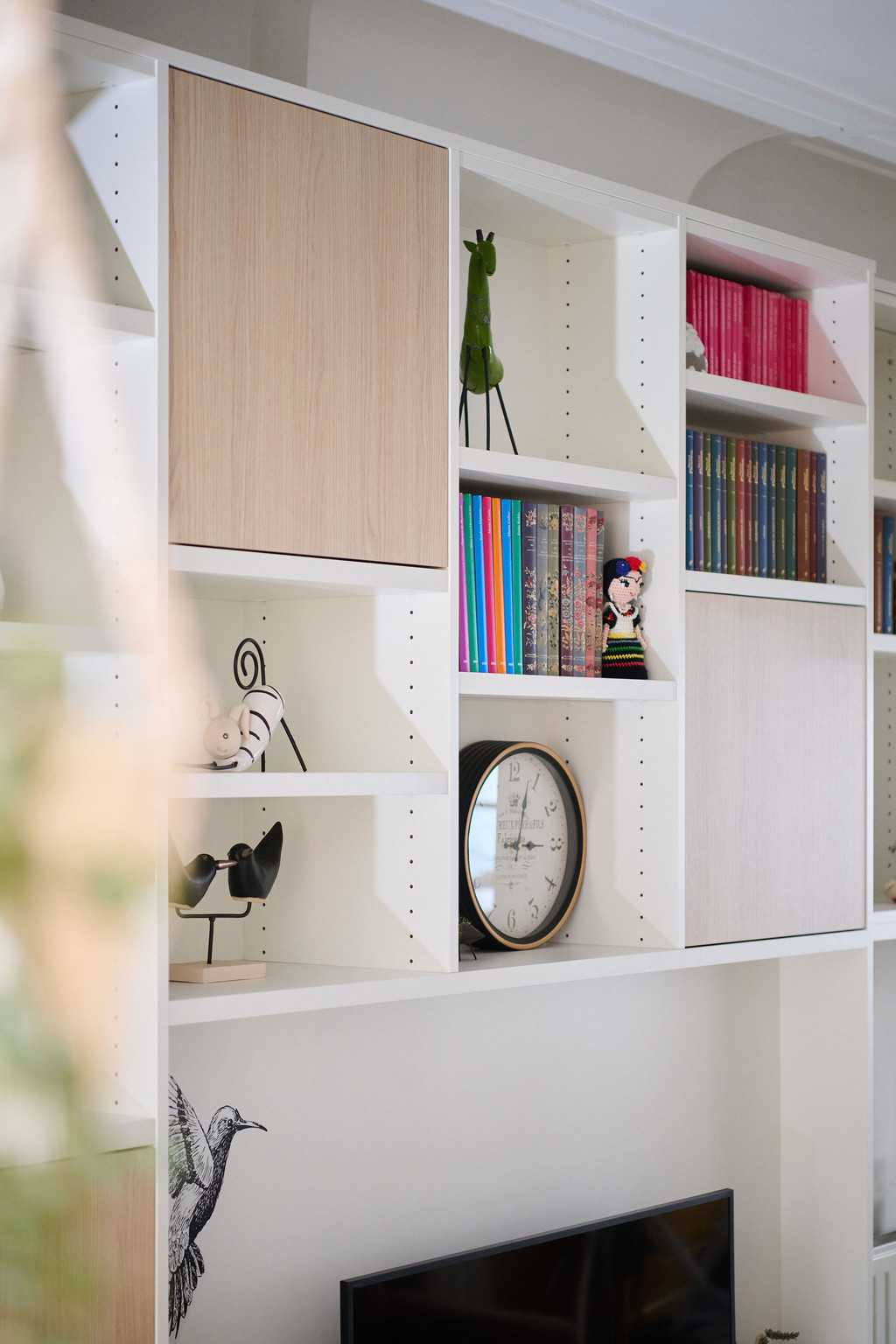Détail d’un meuble TV blanc sur mesure avec niches ouvertes et fermées, livres, horloge et objets de décoration