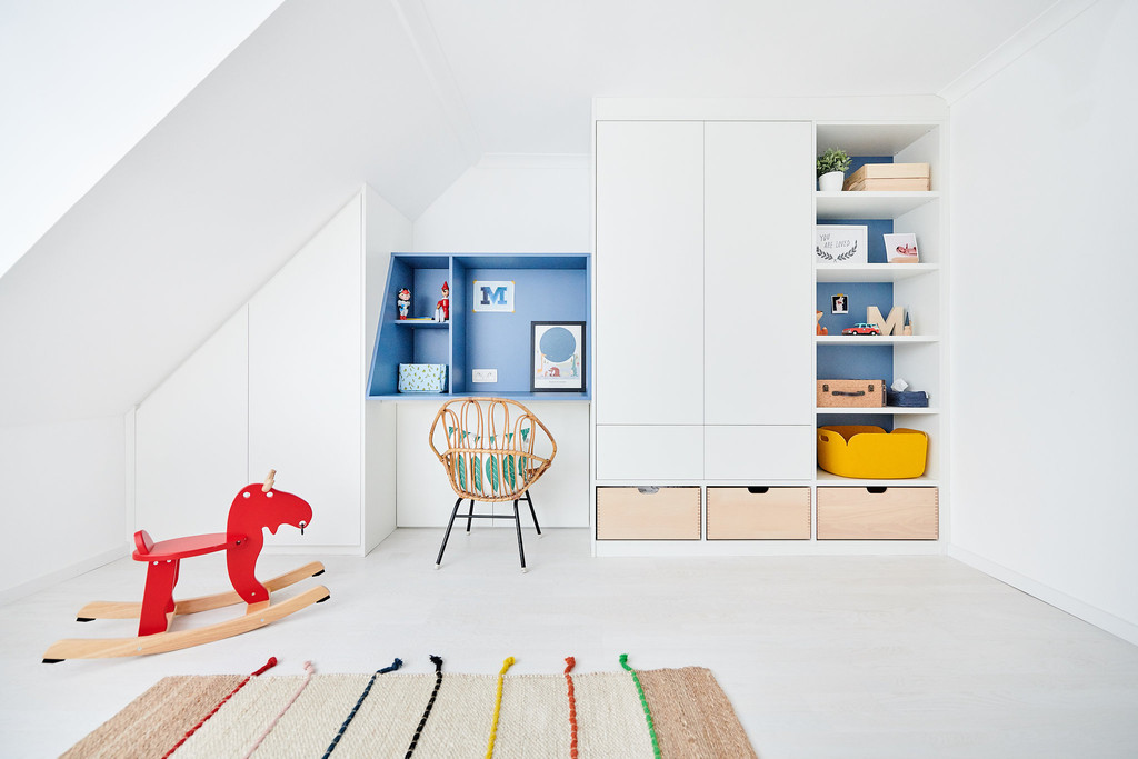 Espace de rangement et bureau intégré pour chambre d'enfant, avec niches bleues et tiroirs en bois clair sous pente.