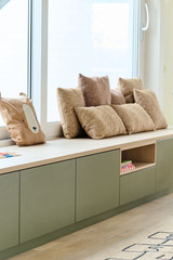 Banquette verte sur mesure avec coussins beiges sous une fenêtre et niche de rangement ouverte