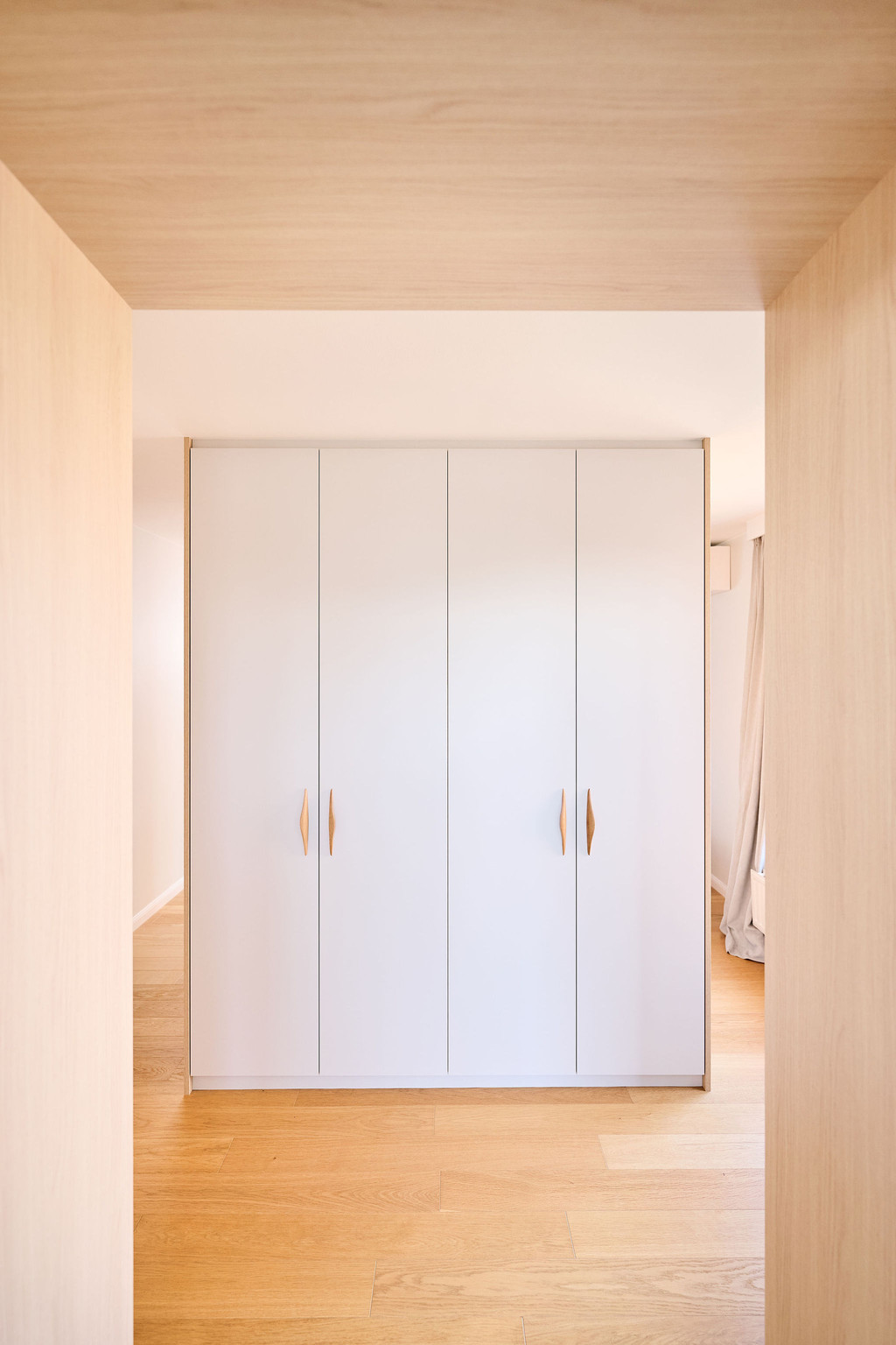 Placard sur mesure utilisé comme séparateur de pièce avec portes blanches et poignées en bois dans une chambre