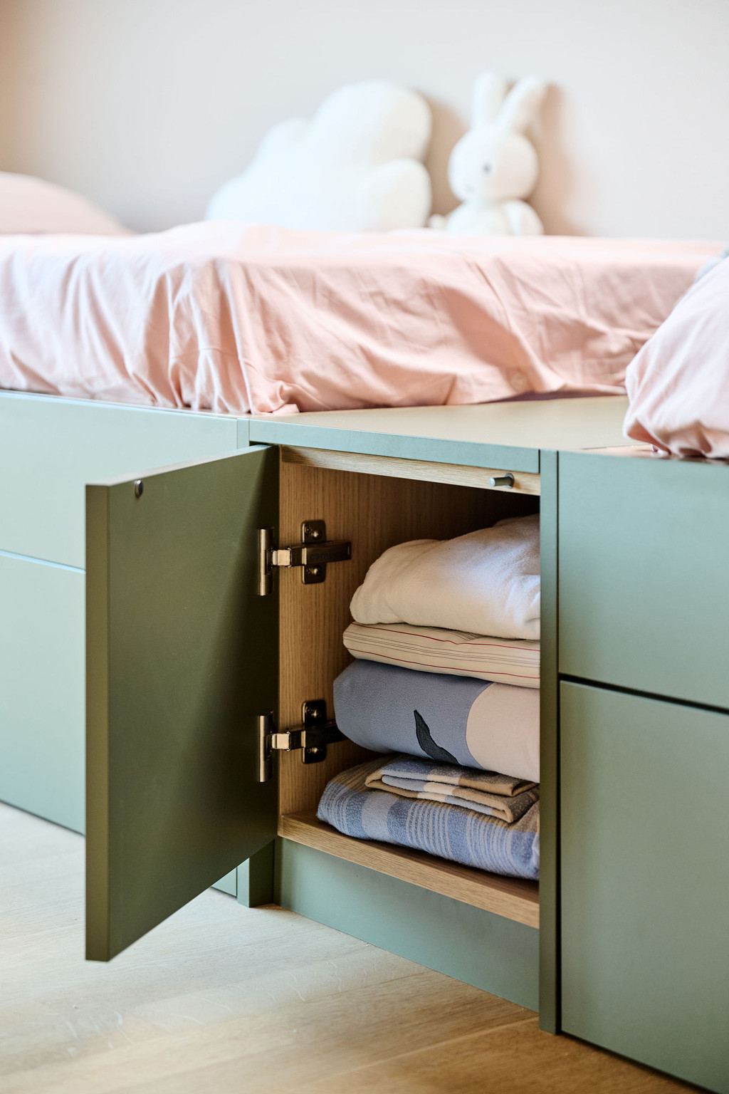 Placard de rangement ouvert sous un lit vert sur mesure avec couvertures soigneusement pliées