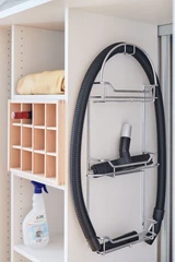 Accessoires de rangement sur mesure pour buanderie, incluant un support pour tuyau d'aspirateur et des étagères pour produits de nettoyage.