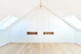 Dressingkast op maat onder schuin dak met open nissen en witte deuren voor een minimalistische uitstraling.