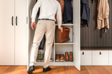 Man in beige broek en wit hemd plaatst een jas in een open witte vestiairekast op maat met vakken voor tassen en schoenen