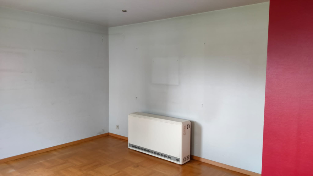 Mur vide avec convecteur dans une pièce au parquet clair et une paroi rouge visible à droite