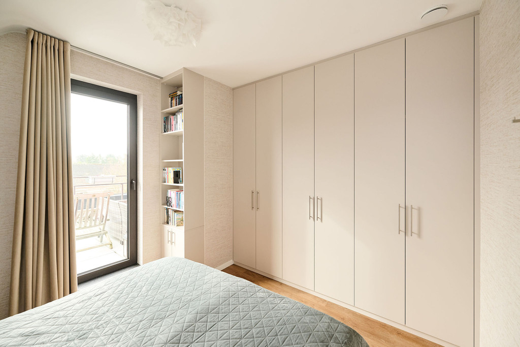 Dressing sur mesure avec portes en tons clairs et niches ouvertes intégrées pour livres, combinant rangement et espace décoratif dans une chambre lumineuse, réalisé par Camber