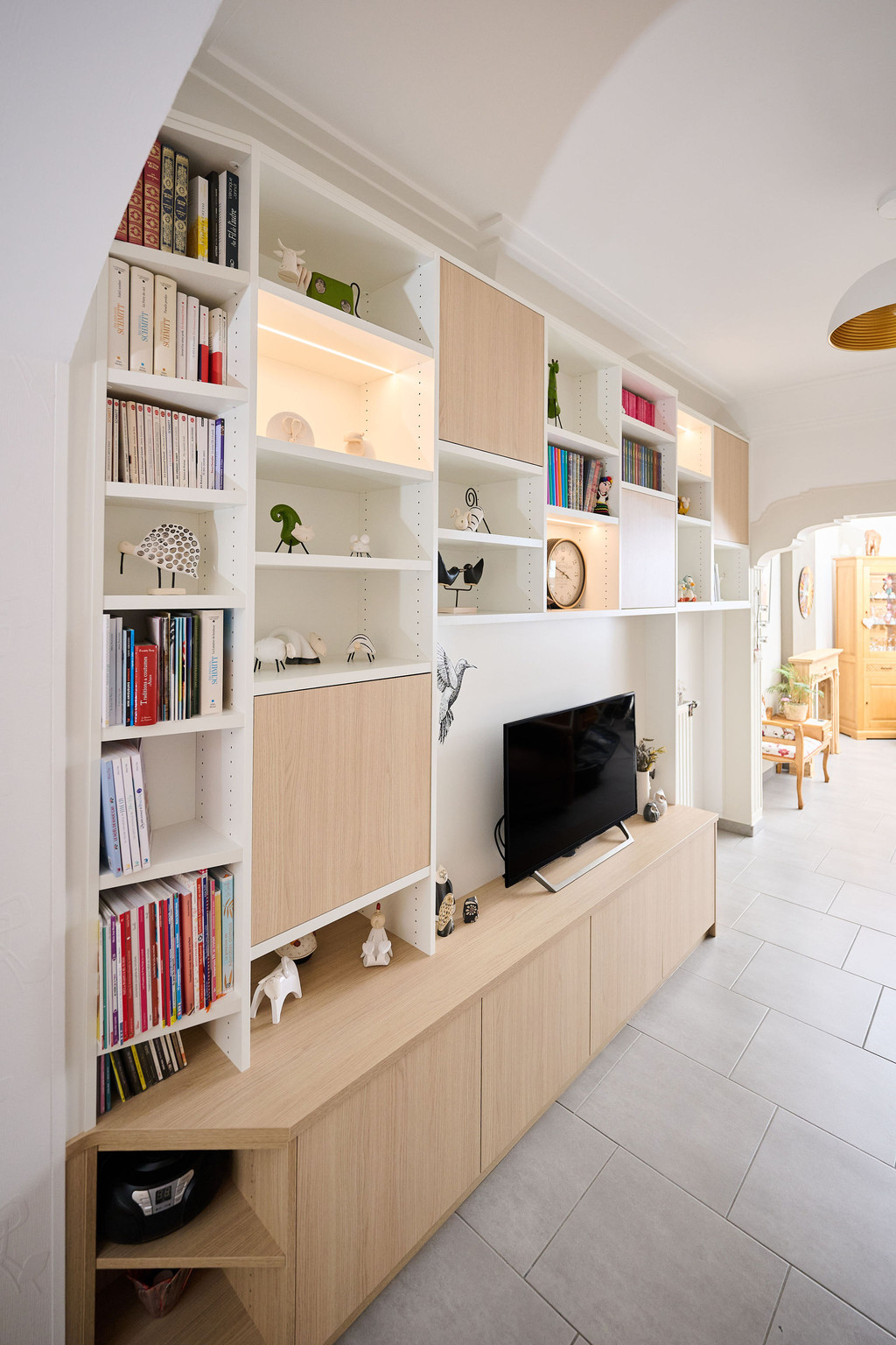 Meuble TV sur mesure avec niches ouvertes et fermées, livres et décorations dans un salon lumineux