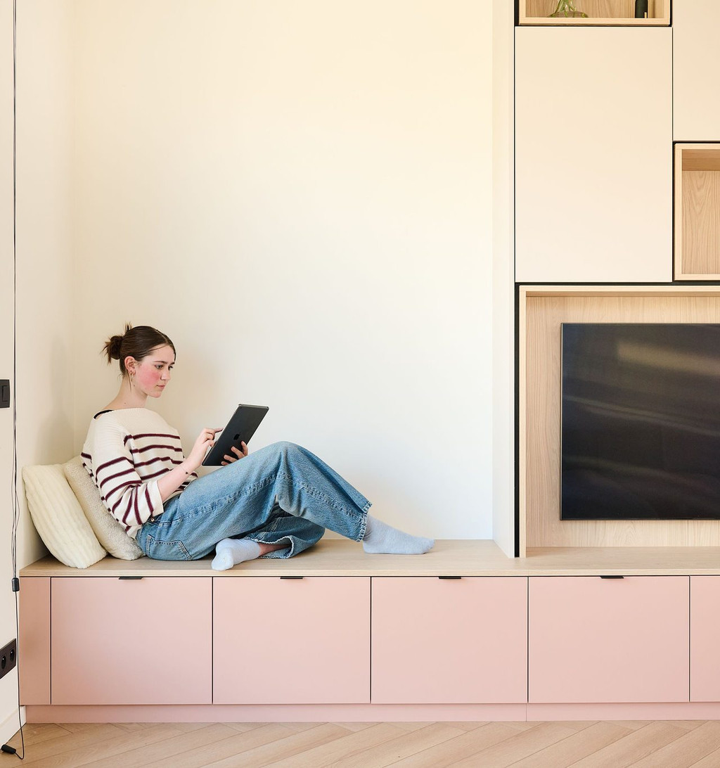 Femme assise sur un banc intégré à un meuble TV sur mesure avec tiroirs de rangement discrets