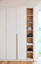 Ingebouwde witte dressingkast op maat met open houten vakken voor sportaccessoires, boeken en schoenen.