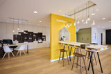 Espace d’accueil avec table haute et chaises dans un showroom Camber avec mur jaune et rangements sur mesure