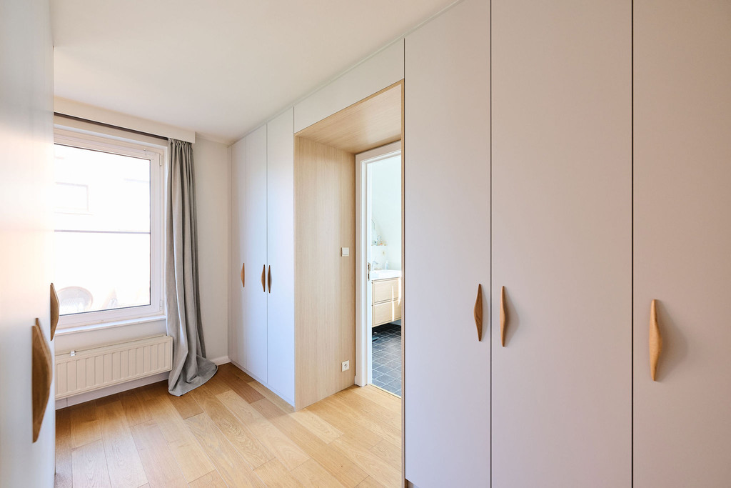 Dressing sur mesure avec portes blanches et finitions bois autour d’une ouverture dans une chambre lumineuse