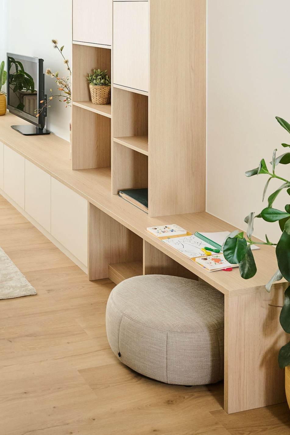 Meuble sur mesure clair avec bureau intégré, étagères ouvertes et pouf dans un salon