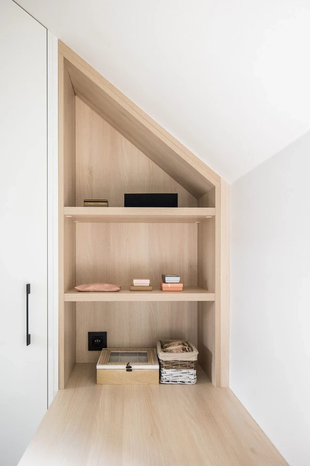 Étagères sur mesure sous pente en bois clair, offrant un rangement optimisé pour divers objets avec un design élégant.