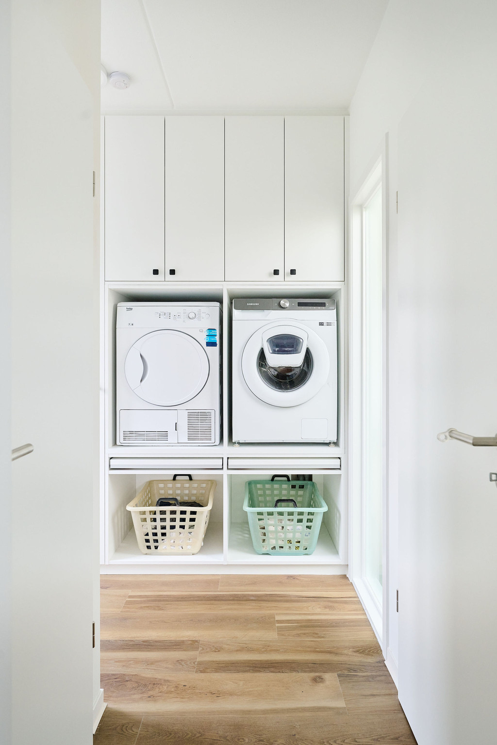 Espace de buanderie sur mesure avec lave-linge, sèche-linge et paniers de rangement.