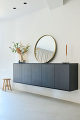 Meuble bas de salon sur mesure avec miroir rond, décoré de plantes et accessoires, dans un salon moderne.