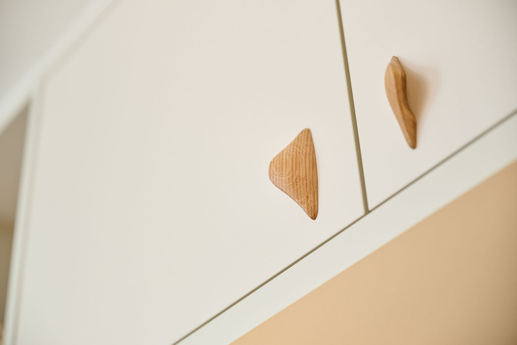 Gros plan sur poignées en bois sculpté fixées sur des portes de placard blanc, ajoutant une touche naturelle et élégante.