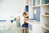 Chambre d'enfant sur mesure avec bureau en bois, tiroirs bleus, bibliothèque ouverte et lit, où un garçon dessine à son bureau
