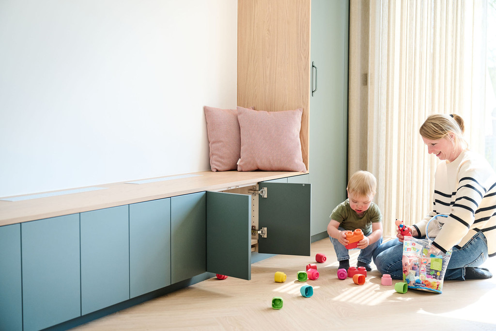 Banquette sur mesure verte avec coussins et armoires basses ouvertes dans une pièce lumineuse avec jouets