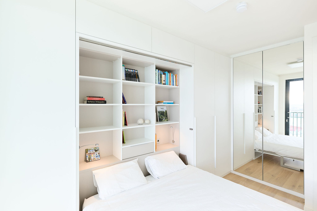 Opklapbed met op maat gemaakte kast met open rekken en verlichting, witte afwerking in een moderne slaapkamer.