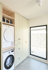 Vue d’ensemble d’une buanderie Camber sur mesure avec machine à laver et sèche-linge en colonne, réfrigérateur intégré, placards fermés et niches ouvertes dans un aménagement fonctionnel