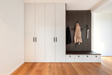Hall d’entrée épuré avec armoire vestiaire intégrée, banc en bois avec tiroirs de rangement et patères murales pour manteaux et accessoires, dans un style moderne.