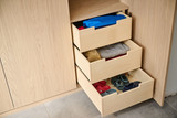 Tiroirs en bois clair avec vêtements pliés et rangés de manière organisée dans un vestiaire sur mesure.