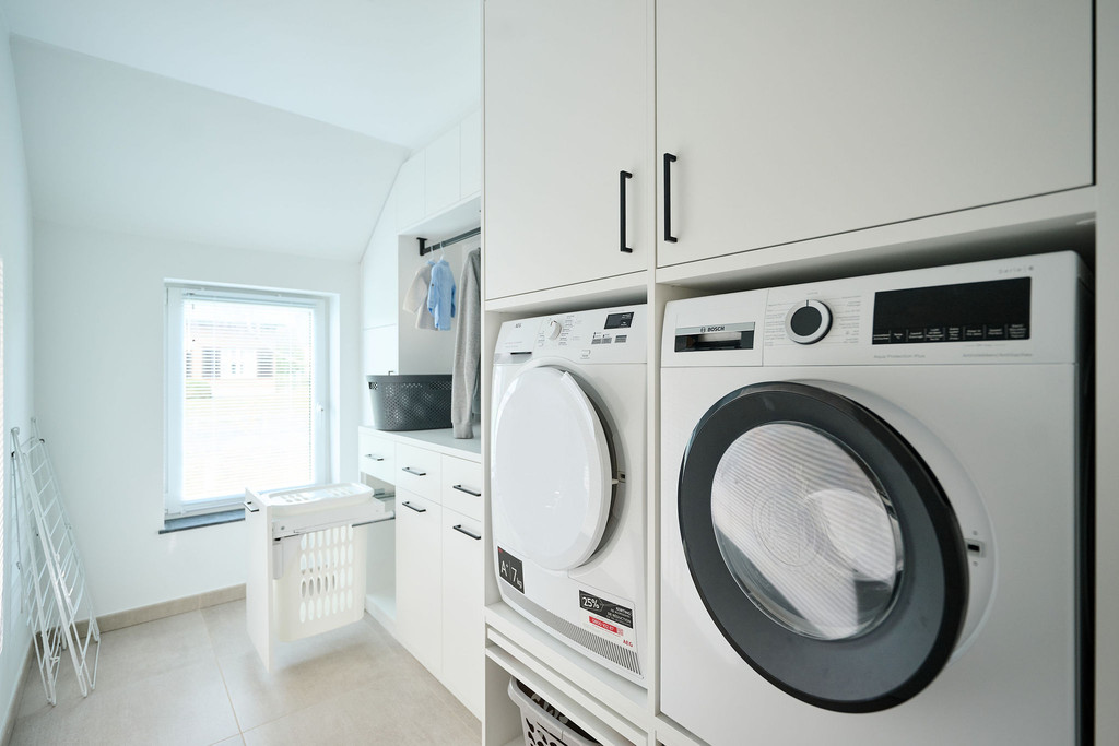 Op maat gemaakte wasruimte met wasmachine en droger, inclusief opbergruimte voor wasmanden.