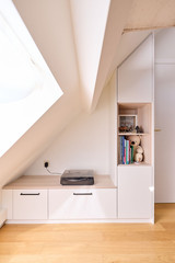 Meuble bas sur mesure sous pente avec tiroirs, niche ouverte et plateau en bois dans une chambre d’enfant lumineuse