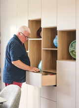 Guido opent een lade van een wandkast op maat met witte fronten en open houten nissen voor decoratie