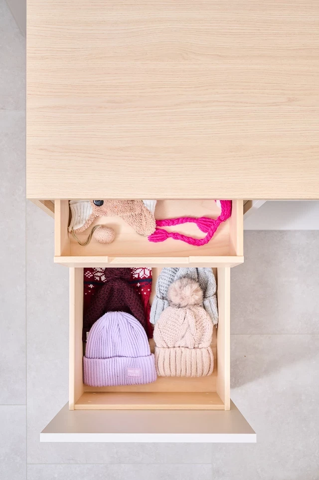 Tiroir sur mesure avec des bonnets et accessoires en laine soigneusement rangés dans un meuble d'entrée en bois clair.