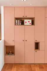 Armoire sur mesure rose avec des niches ouvertes en bois contenant des livres, une décoration dorée et un dessin encadré. Un design élégant et fonctionnel pour un intérieur organisé.