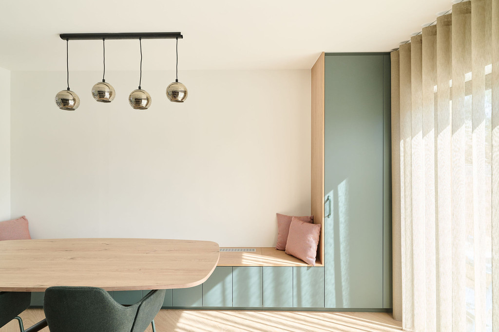 Coin repas lumineux avec banquette sur mesure verte, coussins roses et armoire intégrée