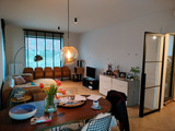 Salon avec mur vide, meuble bas blanc, petite télévision et table ronde en bois au premier plan