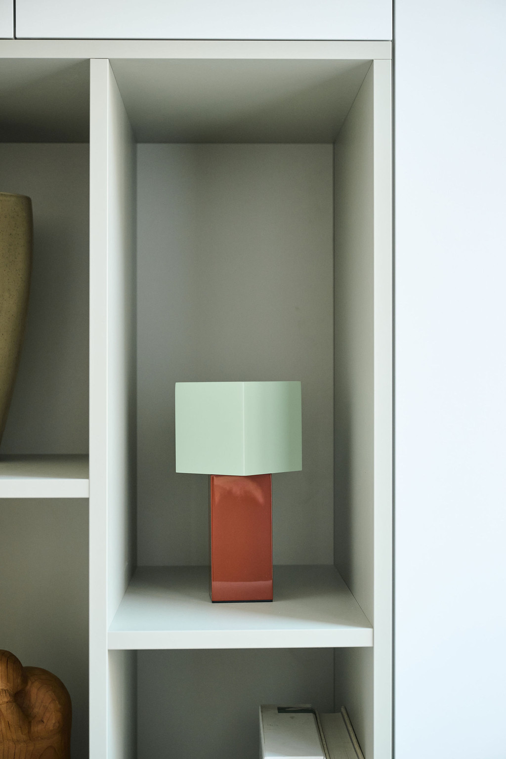 Gros plan sur une petite lampe à abat-jour vert et base rouge dans une niche ouverte d’un meuble blanc